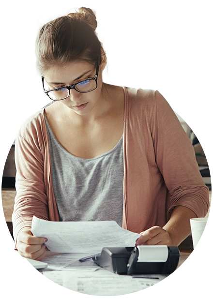 mulher com folhas nas mãos e na mesa, com calculadora ao lado, representando controle de contas a pagar e receber